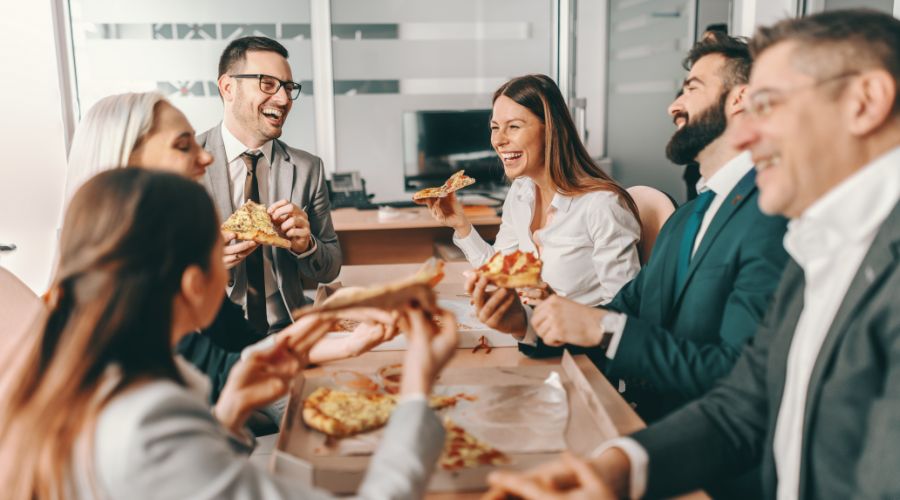 group of coworkers laughing and eating pizza