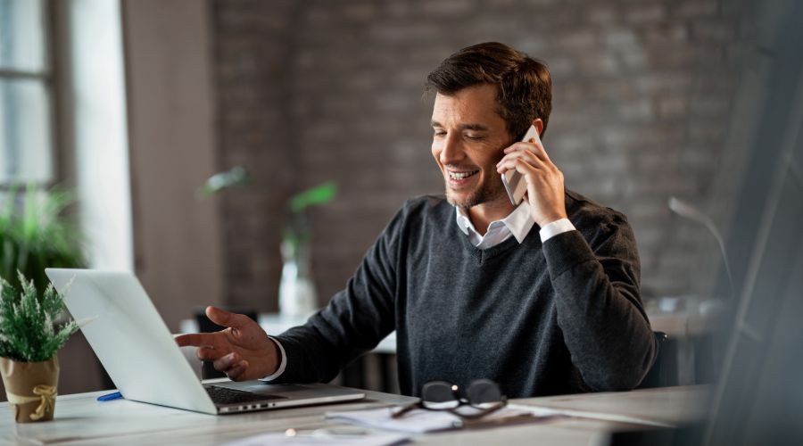 Small business owner talking to his payroll provider on the phone while reviewing info on his laptop